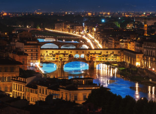  panoramic view of the city at night, with the famous bridge in florence visible from above. the river is flowing through it, and there's an illuminated bridge that connects to buildings on both sides. on one side of the photo, you can see tall buildings, while the other half shows greenery and trees. there are cars driving along the road near the water, adding movement to the scene.