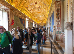 A group of tourists exploring the ornate hallway filled with colorful murals and intricate statues, with an intricately painted ceiling that includes various ancient figures and symbols, within the Sistine Chapel at the Vatican.