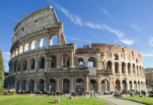 The Colosseum in Rome, Italy is one of the most famous historical buildings and architectural wonders.,a photo of the ancient building stands tall against blue sky with green grass at its base. people can be seen walking around or sitting on horse-drawn carriages to visit it.