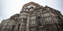 A wide-angle shot of the grand facade of the cathedral in Florence, Italy, showcasing its intricate geometric patterns and towering dome against an overcast sky.