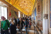 A group of tourists exploring the ornate hallway filled with colorful murals and intricate statues, with an intricately painted ceiling that includes various ancient figures and symbols, within the Sistine Chapel at the Vatican.