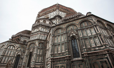 A wide-angle shot of the grand facade of the cathedral in Florence, Italy, showcasing its intricate geometric patterns and towering dome against an overcast sky.